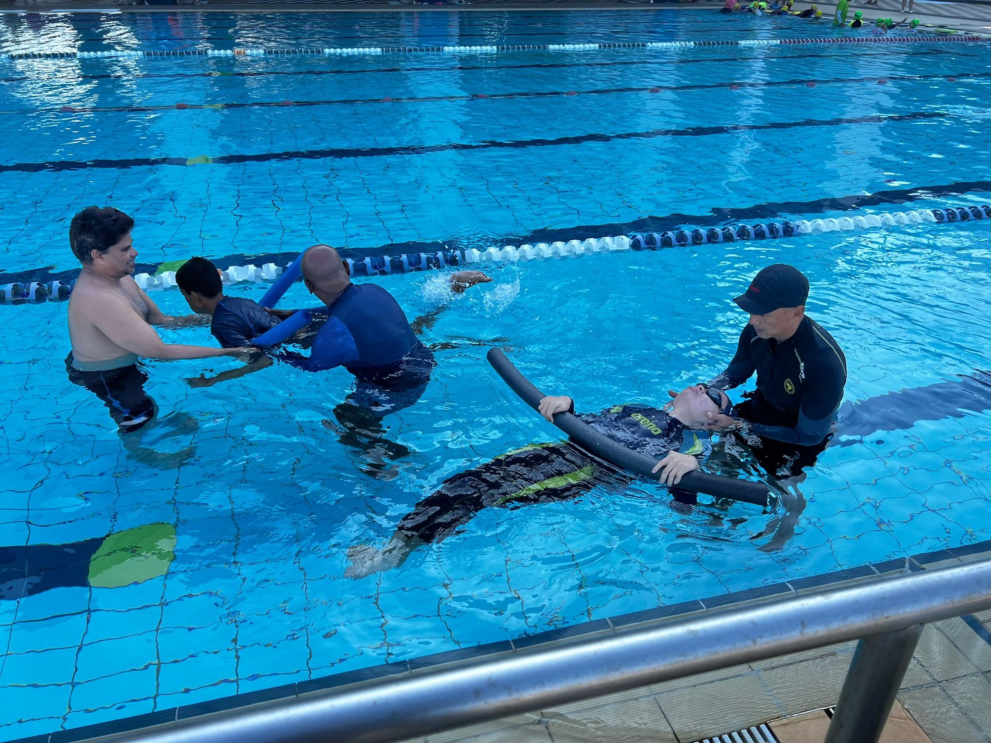 Photo of Para Sport Academy two swim coaches guiding two learners in the swimming pool using floatation aids known as noodles